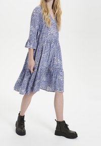 Abito blu con stampa floreale, scollo a V, maniche a tre quarti svasate e gonna a strati. Abbinato a stivali neri con lacci alla caviglia.