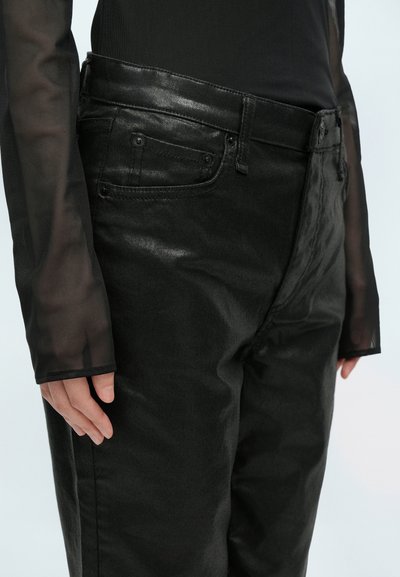Čierne džínsy s hladkou textúrou, s vysokým pásom, klasickým dizajnom s piatimi vreckami a jemným leskom. Vedľa priehľadného topu s dlhým rukávom.