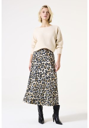 Un pull en tricot beige associé à une jupe imprimé léopard de longueur mi-mollet. La tenue est complétée par des bottes noires à talons hauts jusqu'aux genoux.