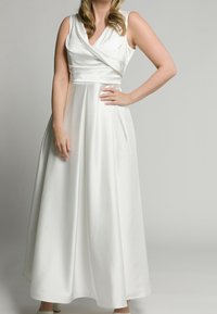 Vit maxiklänning med inwrapad bodice, V-ringning och ärmlös design. Har ett flödande, slätt tyg och dolda sidofickor.