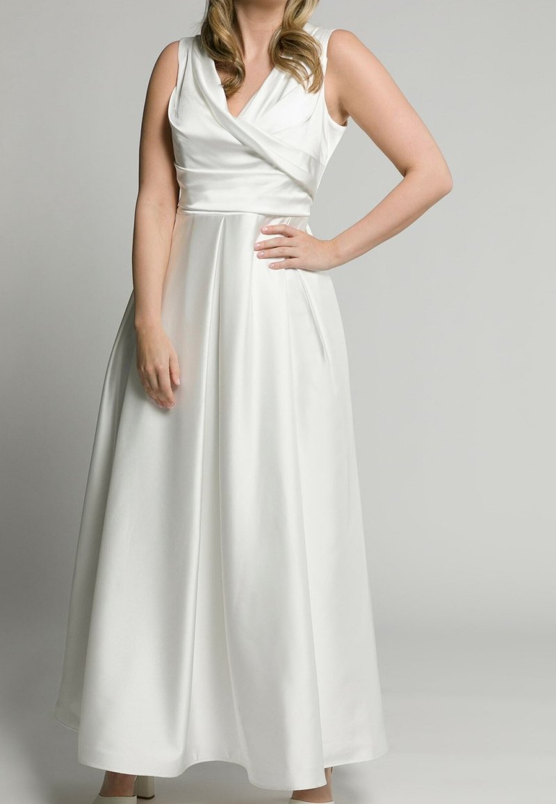 Vit maxiklänning med inwrapad bodice, V-ringning och ärmlös design. Har ett flödande, slätt tyg och dolda sidofickor.