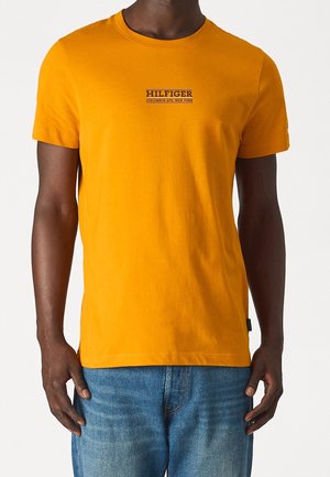 Gelbes Baumwoll-T-Shirt mit kurzen Ärmeln, auf der Brust mit dem schwarzen Logo-Text "HILFIGER COLUMBUS AVE. NEW YORK" versehen. Slim Fit Design.