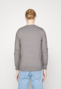 Gray long-sleeve sweater with a round neckline and ribbed hem, paired with light blue denim jeans. Smooth texture, fitted design.