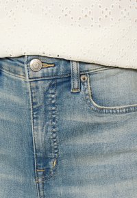 Ljusblå denimjeans med en blekt finish, försedda med en silverknapp och kontrasterande sömmar, i kombination med en topp av strukturerad vit tyg.