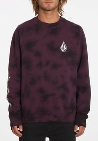 Pikétröja i mörklila tie-dye med en frontlogga och kontrasterande svarta accenter på ärmarna. Tillverkad av mjukt tyg.