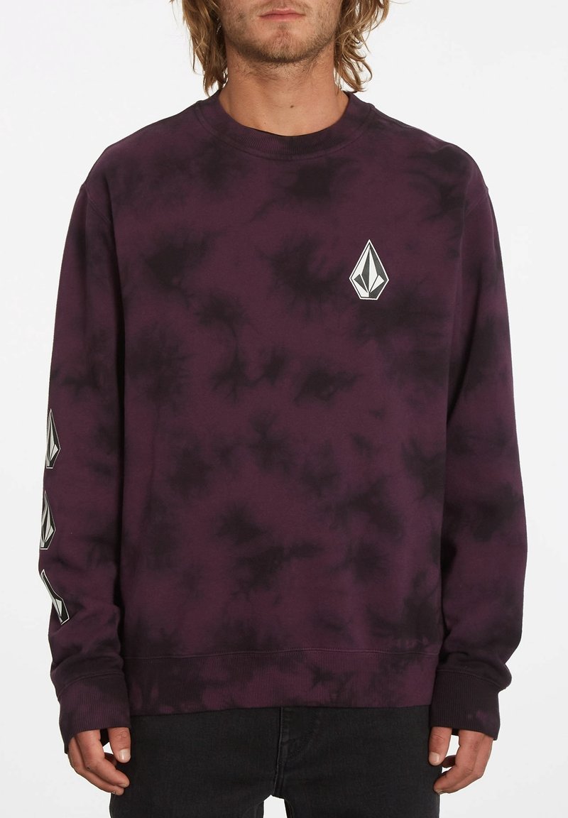 Pikétröja i mörklila tie-dye med en frontlogga och kontrasterande svarta accenter på ärmarna. Tillverkad av mjukt tyg.
