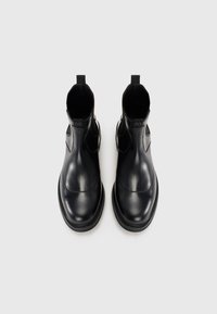 Botas Chelsea de cuero negro con acabado suave, paneles laterales elásticos, tiradores y un diseño de punta redonda. Costuras de contraste visibles.