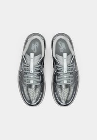 Sneakers Nike Air con una finitura grigia lucida, dettagli in rete stampata, lacci grigi e una linguetta imbottita. Presenta un logo sulla soletta.