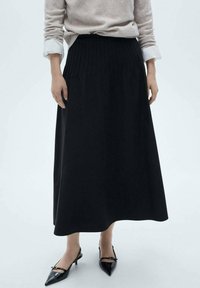 Sort, plisseret maxiskørt lavet af blødt stof, båret med en lysegrå sweater og sorte spidse hæle. Glat tekstur, gulvlængde design.