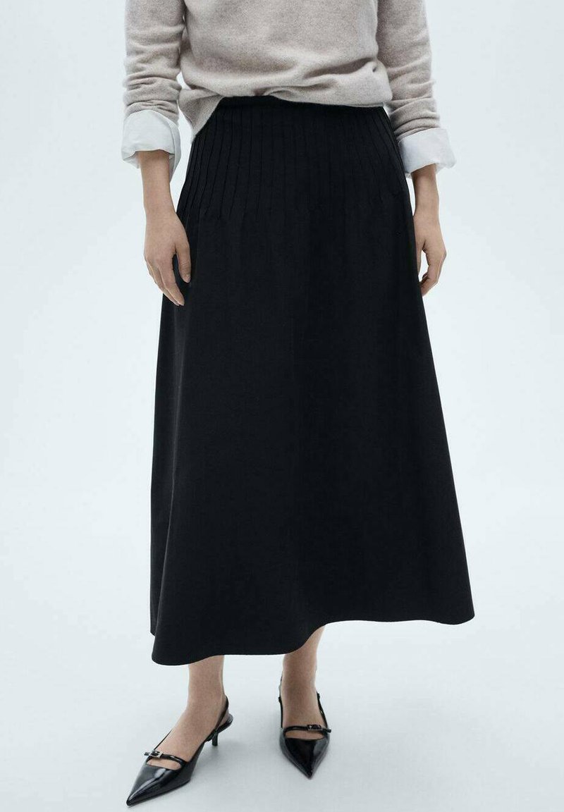 Sort, plisseret maxiskørt lavet af blødt stof, båret med en lysegrå sweater og sorte spidse hæle. Glat tekstur, gulvlængde design.