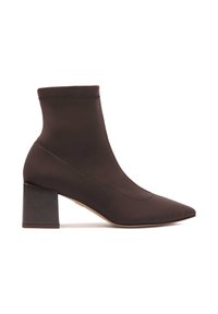 Botas de tobillo marrones hechas de un material suave con punta afilada y tacón cuadrado. Cuenta con un cañón elástico para un ajuste ceñido.