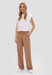 Haut blanc à manches courtes associé à un pantalon marron taille haute, plissé, et des baskets blanches. Tissu lisse avec une coupe décontractée.