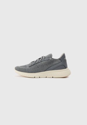 Zapatillas deportivas grises con parte superior de tejido texturizado, suela de goma gris claro y cordones negros. Incluyen un logotipo en el lateral.
