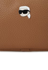 Borsa in pelle marrone con una texture distintiva e una spilla prominente di un personaggio dei cartoni animati che indossa occhiali da sole neri e una fascia bianca.