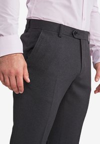 Pantaloni ajustați de culoare gri închis, dintr-un material texturat, cu buzunare laterale și închidere cu buton în față. Asortați cu o cămașă de culoare roz deschis la manșetă.