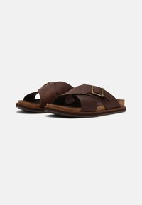 Sandales en cuir marron avec deux larges sangles croisées, une boucle en métal réglable, une semelle intérieure en liège profilée et une semelle extérieure en caoutchouc texturé.