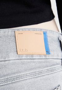 Traperice svijetlosive boje s kožnom oznakom svijetlosmeđe boje i plavim akcentima na kojoj piše "l.t.b - Live to Be - Studio Designed."