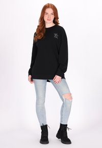 Felpa nera con maniche lunghe, collo a giro e dettaglio ricamato. Indossata con jeans skinny strappati blu chiaro e stivali neri con lacci.