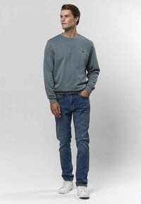 Szara bluza z okrągłym dekoltem i prążkowanymi mankietami, zestawiona z obcisłymi niebieskimi dżinsami i białymi trampkami. Prosty, casualowy design, bez wzorów i dodatków.