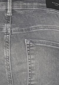 Jeans de ganga cinza com um efeito desbotado, costuras visíveis e um bolso traseiro. Etiqueta com "Vero Moda" está presa à cintura.