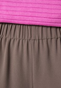 Ljusrosa ribbad topp som är kombinerad med byxor med elastiskt midjeband i brunt; tyget är mjukt med en slät yta och har rynkade detaljer vid midjan.