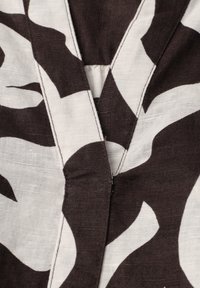 Gros plan d’un tissu noir et blanc avec un motif de feuilles audacieux et des coutures visibles le long de la couture centrale et de la zone du col.