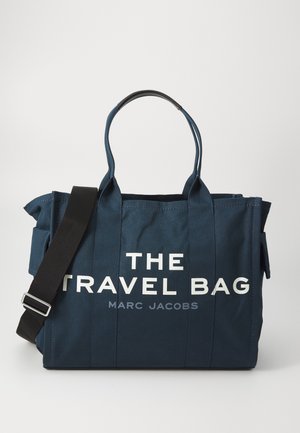 Bolsa de viaje de lona color azul marino con correas negras, con texto en blanco audaz "LA BOLSA DE VIAJE" y "MARC JACOBS" impresos en la parte frontal.