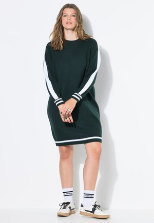 Vestido de punto verde con acentos de rayas blancas en las mangas, puños acanalados y dobladillo, combinado con calcetas blancas y zapatillas negras. Diseño y ajuste casual.