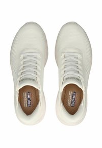 Baskets blanches de sport avec un dessus en maille texturée, un design à lacets et une semelle intérieure marron, dotées d'une semelle arrondie et rembourrée.