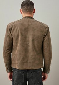 Chaqueta de piel sintética marrón con acentos acolchados en los hombros y cremalleras plateadas, con un diseño ajustado y una textura suave.