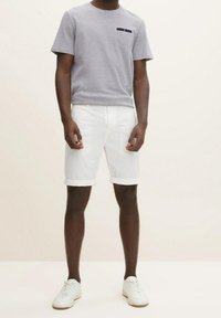 Maglietta grigia a maniche corte con dettaglio di tasca blu navy, abbinata a pantaloni corti bianchi arrotolati. Sneakers bianche completano l'outfit.