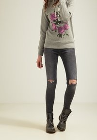 Felpa grigia con stampa floreale, abbinata a jeans skinny strappati grigi scuri e stivali grigi con lacci. Design semplice con vestibilità casual.