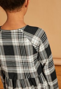 Czarna i biała sukienka w kratę z długimi rękawami, okrągłym dekoltem i marszczoną talią. Materiał wydaje się miękki o gładkiej teksturze.