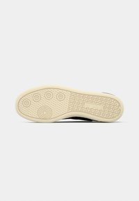 Semelle de chaussure avec une bande de roulement en caoutchouc beige présentant des motifs circulaires à l'avant et des motifs géométriques avec un logo de marque sur la zone du talon.