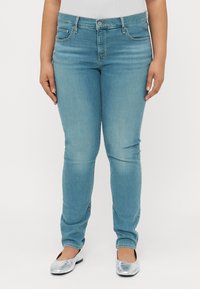 Vaqueros ajustados de color azul claro, confeccionados en denim, con un diseño clásico de cinco bolsillos, con cierre de botón y una textura ligeramente desgastada.