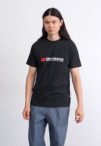Sort bomulds t-shirt med et markant rødt og hvidt "New Balance" logo. Enkel design med rund hals og korte ærmer.