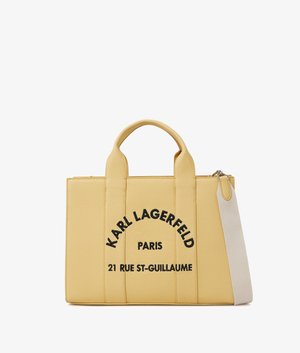 Gele gestructureerde draagtas met twee handvatten, een witte schouderriem en zwarte tekst "Karl Lagerfeld Paris 21 Rue St-Guillaume" aan de voorkant.