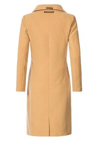 Lange beige jas, gemaakt van een soepele stof, met een kraag, rechte snit en een enkele split aan de achterkant. Geen zichtbare zakken.