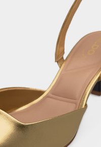 Close-up of a gold metallic slingback shoe with a block heel and cushioned beige insole.