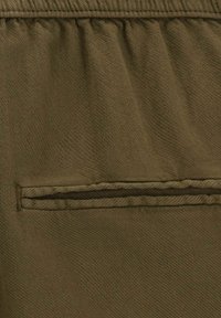 Tissu vert olive avec une poche arrière à finition soignée et un détail de couture subtil, présentant une texture lisse et un design minimaliste.