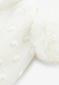 Hvid strikket hue med et tekstureret mønster og en stor, blød pom-pom detalje. Lavet af blødt, varmt materiale. Rund form.