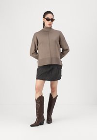 Beige gestrickter Rollkragensweater, cropped Design; dunkelblaue Jeans-Minirock; braune Cowboy-Stiefel mit spitzer Zehe und geprägten Blumenmotiven.