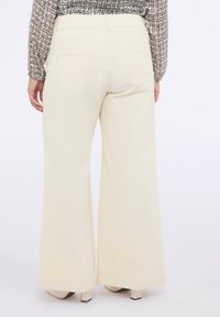 Pantaloni larghi color crema con una trama liscia, dotati di due tasche posteriori e una vita elasticizzata per il massimo comfort. Cuciture chiare lungo le cuciture.