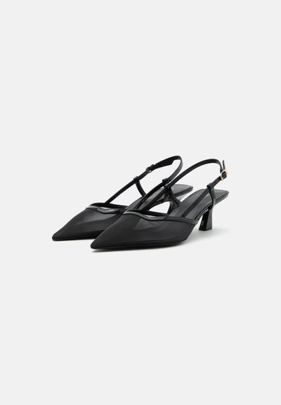 Escarpins slingback noirs à bout pointu, avec fines brides, petits talons blocs bas et petites boucles sur fond blanc uni.