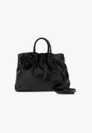 Sort læderhåndtaske med tophank, en dekorativ rose foran og en aftagelig skulderrem, der ligger sammenrullet ved siden af.