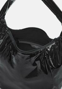 Bolso de mano de charol negro con forma redondeada, que cuenta con un cierre con cremallera y un forro interior suave, resaltando los detalles de costura.