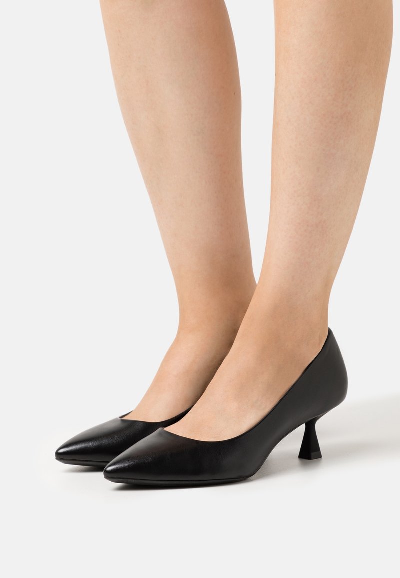 Chaussures à talons hauts en cuir noir avec un bout pointu et un talon courbé, présentant une texture lisse et un design simple et élégant.