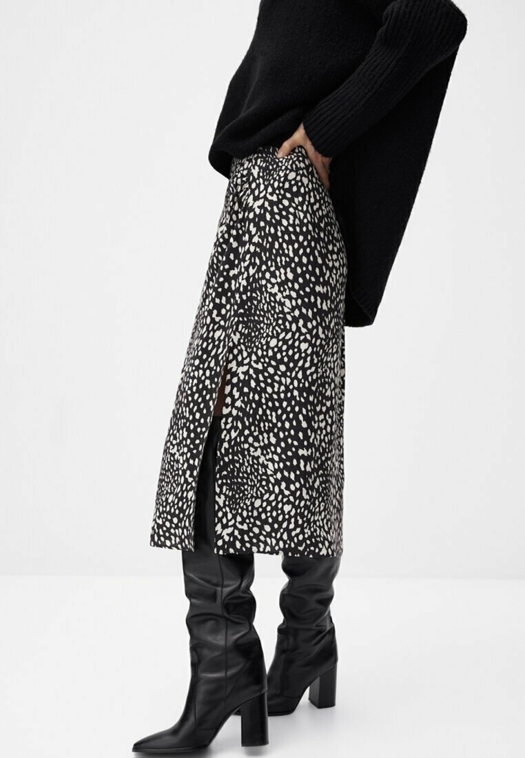 Jupe mi-longue à motif noir et blanc en tissu, avec des fentes latérales, associée à des bottes en cuir noires montantes jusqu'au genou.