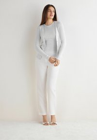 Jasnoszary kardigan z guzikami na dopasowanej prążkowanej bluzce, w połączeniu z białymi spodniami prostymi i białymi sandałami z kokardką.