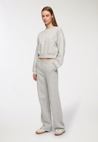 Szara, krótką bluza z długim rękawem i luźnym krojem, zestawiona z dopasowanymi, szerokimi spodniami dresowymi. Miękka faktura tkaniny i elastyczny pas.